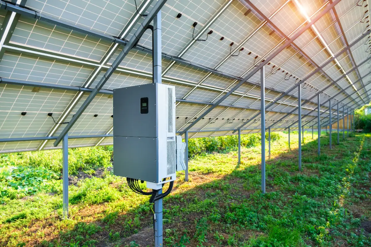 Arazi tipi güneş enerjisi santralinde panel sıralarının altına direğe monte edilmiş ekranlı inverter